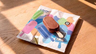 A chocolate-coated ice cream bar rests on a colourful wrapper on a wooden table.