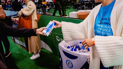 Participante recebe embalagem cartonada de água em área de evento, com cooler da Tetra Pak ao lado, representando a experiência da marca na NaturalTech 2026.