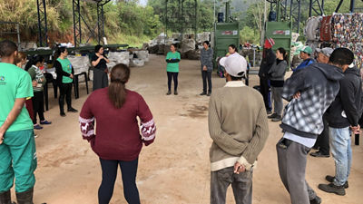 Profissionais reunidos em centro de triagem, com fardos de recicláveis e equipamentos ao fundo, representam a cadeia de reciclagem no Brasil apoiada pela Tetra Pak.