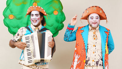 Dois atores caracterizados com roupas típicas nordestinas, maquiagem artística e chapéus de cangaceiro, um deles com sanfona, durante apresentação da peça “Fim Que Vira Começo Que Vira...”, que ensina reciclagem e economia circular a crianças.