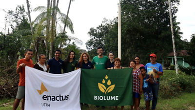 Integrantes do projeto Biolume e moradores da comunidade posam ao ar livre segurando bandeiras da Enactus UFPA e do Biolume, iniciativa vencedora do Vitrine Tetra Pak 2026.