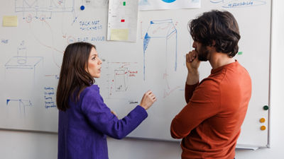 Two people in front of board in conference room