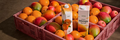 Orange juice and mango nectar cartons surrounded by fresh oranges, mangoes and apples
