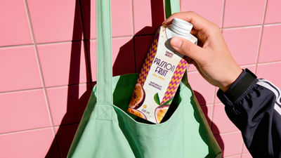 On-the-go juice Hand placing a passion fruit drink carton into a reusable shopping bag