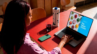 Woman watching a juice webinar on a laptop while drinking juice