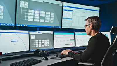 Man monitoring production data across multiple screens in a control room