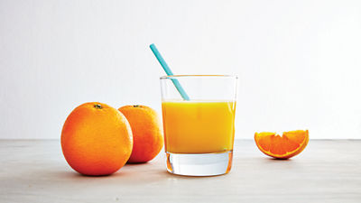 Orange juice in glass with straw and and oranges in the background