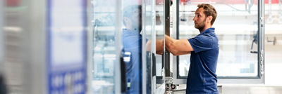 Technician in a blue shirt working on industrial processing equipment in a production facility.