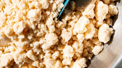 Close-up of crumbly okara soya pulp in a bowl with a scoop.