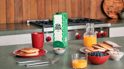 Carton of soya drink on a kitchen counter with breakfast food and orange juice