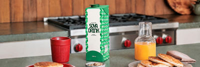 Carton of soya drink on a kitchen counter with breakfast food and orange juice