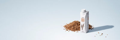 Carton of plant-based brewer's spent grain drink surrounded by grains on a light blue background.