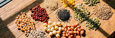 Assortment of beans, lentils, seeds and nuts arranged in small piles on a wooden surface.