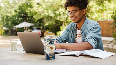 Young man with computer, protein milk in Tetra Prisma Aseptic carton package