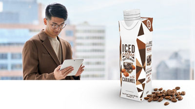 Man med surfplatta, frappuccino-kaffedryck i Tetra Prisma® Aseptic-kartongförpackning