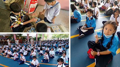 World School Milk Day. Recycling activity.  Children folding used milk cartons before throwing into the bin for recycling
