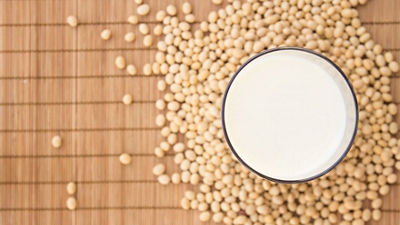 Un verre de lait de soja entouré de graines de soja sur fond brun