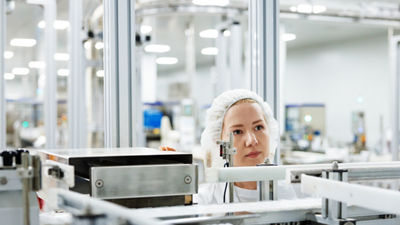 Worker wearing a hairnet inspecting machinery in a food production facility.
