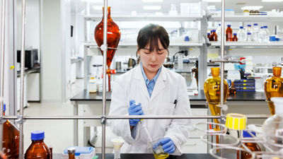 Laboratory employee wearing a white coat and blue gloves handling a sample in a food research laboratory.