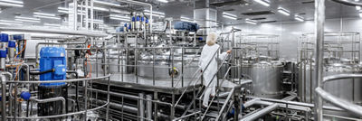 Employee in a white coat climbing stairs among stainless steel processing tanks and pipes.