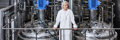 Woman in white protective clothing standing between industrial processing tanks at a Tetra Pak facility.