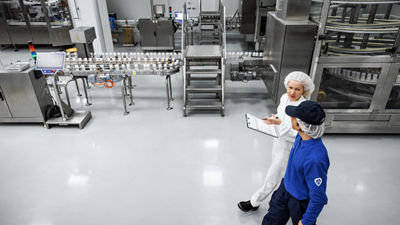Overhead view of two employees walking through a production hall, one holding a tablet