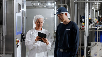 Two employees reviewing a tablet beside a control panel in a processing facility.