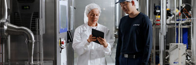 Two Tetra Pak employees reviewing information on a tablet inside an industrial food processing facility.