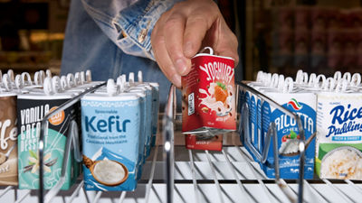 Person selecting a Tetra Reva package from a refrigerated supermarket shelf.