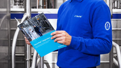 Tetra Pak employee holding an upgrades brochure beside stainless steel processing equipment