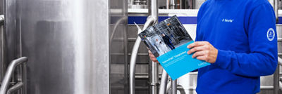 Tetra Pak employee holding an upgrades brochure beside stainless steel processing equipment