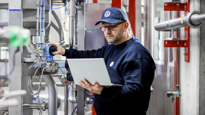 Technician using a laptop while checking equipment among stainless steel pipes