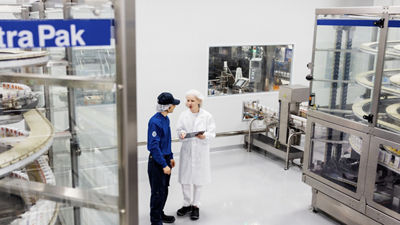 Two employees reviewing a handheld device between Tetra Pak packaging machines