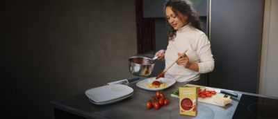 Woman cooking pasta, tomato sauce in Tetra Recart carton package