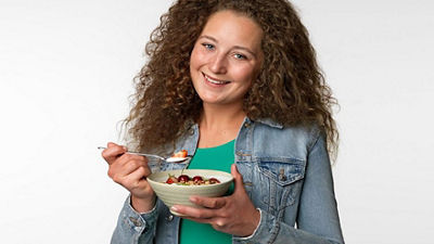 A woman eating yoghurt with berries on top out of a bowl