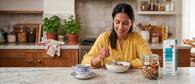 Woman in kitchen making breakfast, cereals and milk in carton package