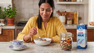 Woman in kitchen making breakfast, cereals and milk in carton package