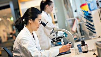 Woman in lab, looking in microscope