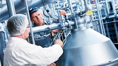  Dos hombres trabajan juntos para hacer funcionar una máquina de gran tamaño en un entorno industrial.