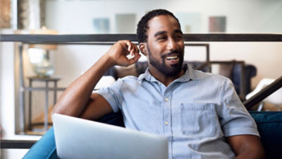 A man sitting comfortably with a laptop, smiling while looking to the side.