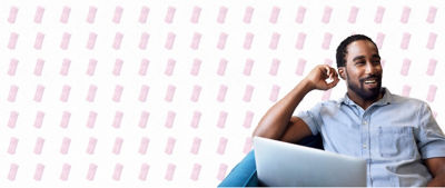 The image shows a smiling man with a beard, wearing a light blue shirt, sitting and relaxing with a laptop on his lap. The background features a pattern of pink carton icons, creating a light and cheerful atmosphere.