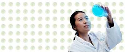 A woman in a lab coat holds an object up to inspect it closely.