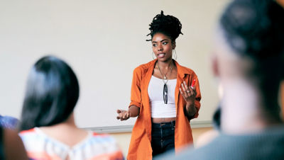 A woman stands at the front of a group of people sharing ideas.