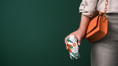 Mujeres sosteniendo un envase de cartón pequeño con fondo verde y el costado de su bolso naranja