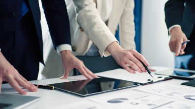 Tablet and charts on a table, fingers pointing at it