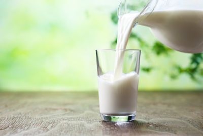 Milk pouring into a glass of milk on brown surface with green background