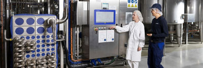 Two workers walking through an industrial processing facility with stainless steel equipment and pipelines