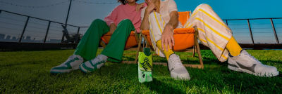 Man and woman sitting in beach chairs on the grass with an RTD alcoholic beverage in carton beside them