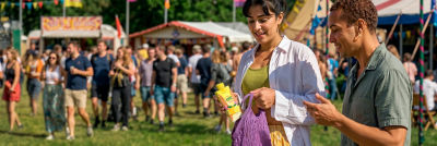 Man and woman at a festival. Woman puts her RTD alcoholic beverage in carton into her bag