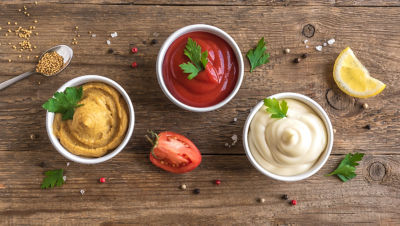 Mustard, ketchup and mayonnaise in bowls on wooden tray